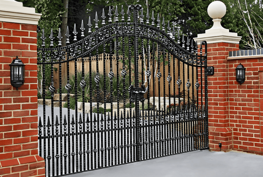 Black iron driveway gates between brick pillars